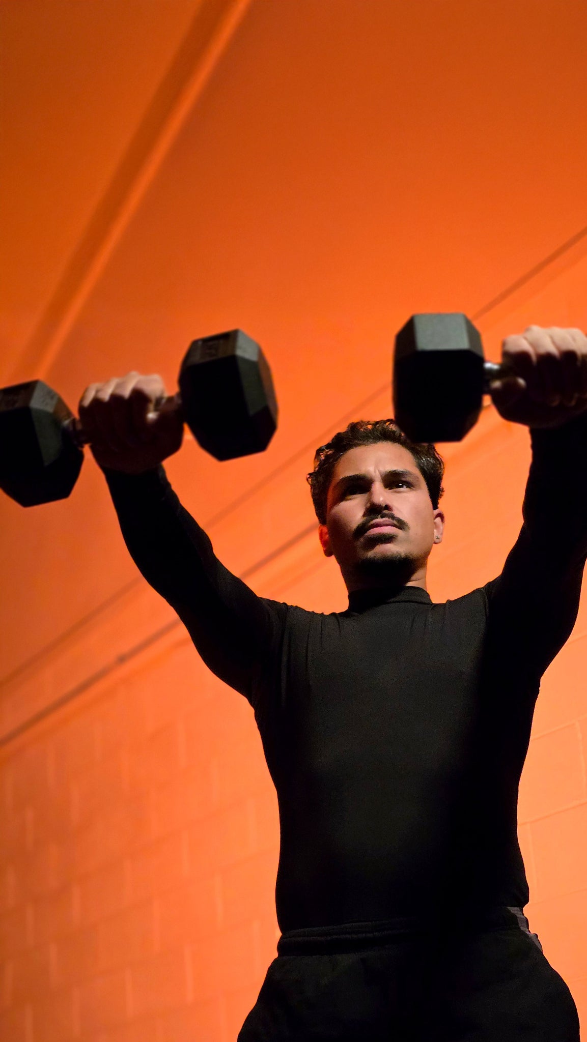 Person lifting dumbbells against an orange background